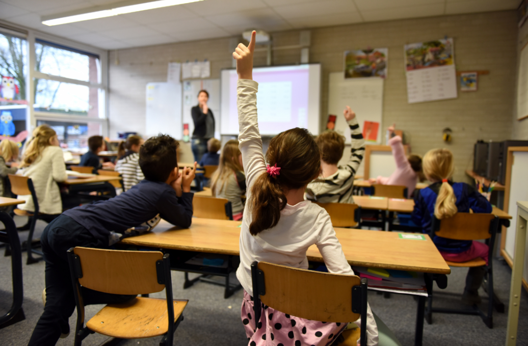 Photo of children in class room with one raising their hand